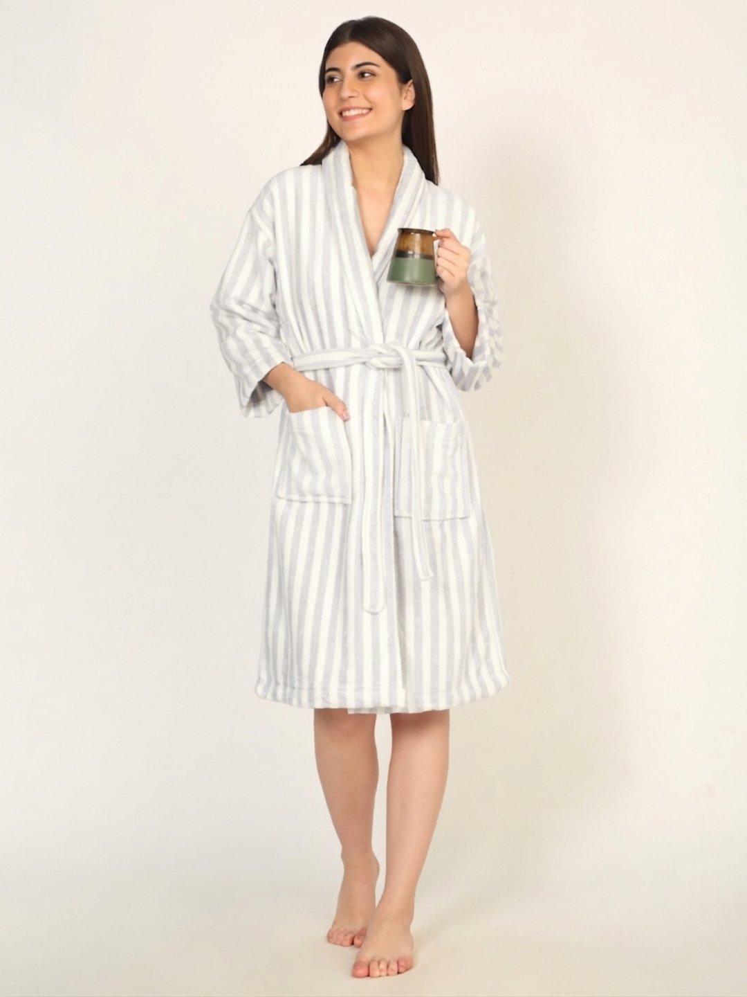 Woman wearing a white and gray striped robe holding a mug on a beige background