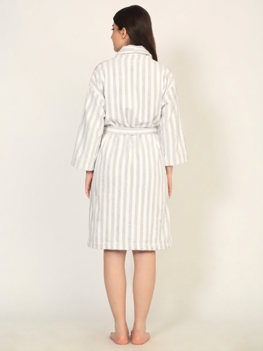 Woman wearing a white and gray striped robe on a plain background