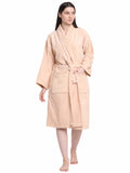 A woman modeling a light peach-colored terry cloth bathrobe with a matching tie belt, standing against a plain white background.