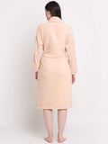A woman viewed from behind wearing a light peach-beige terry cloth bathrobe with a shawl collar and waist tie, standing against a plain white studio background.