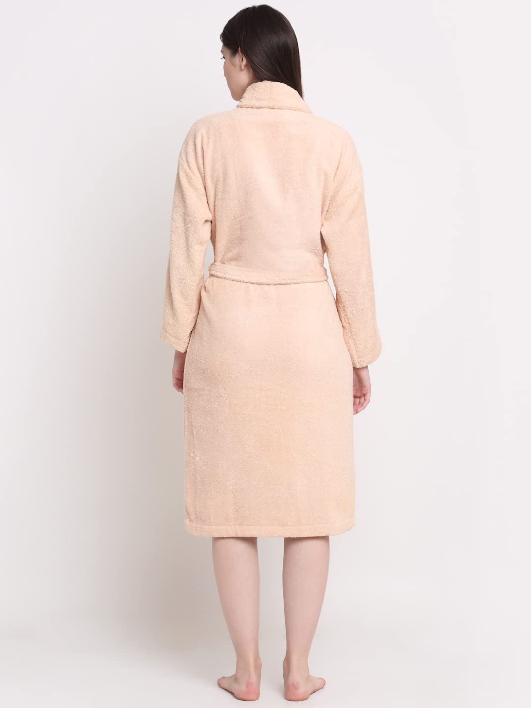 A woman viewed from behind wearing a light peach-beige terry cloth bathrobe with a shawl collar and waist tie, standing against a plain white studio background.