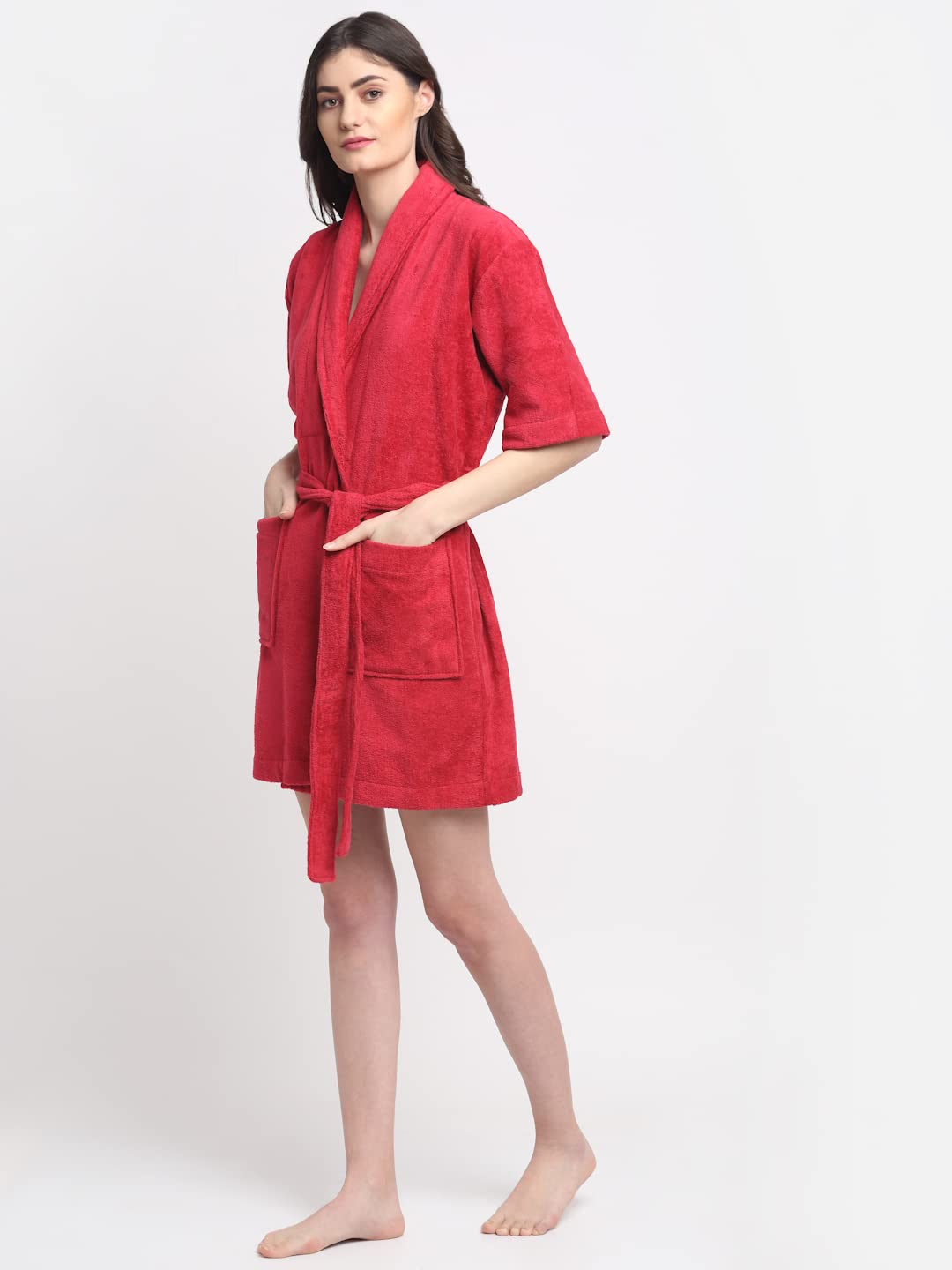 A woman modeling a short-sleeved red bathrobe with a tie waist and front pockets, standing against a plain light gray studio background.