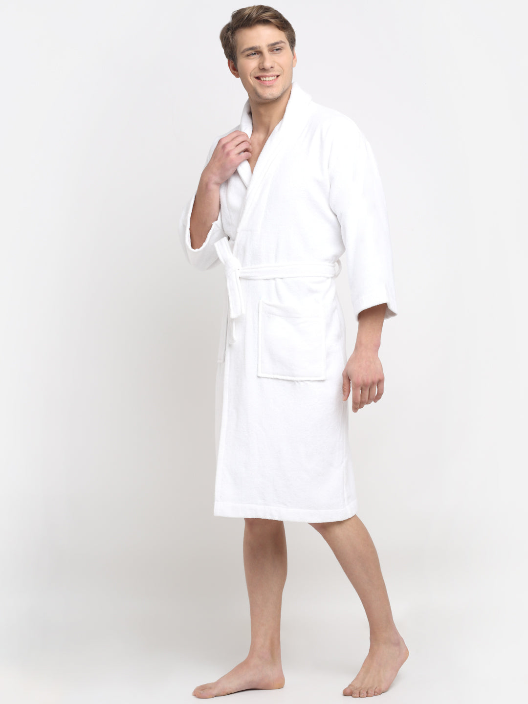 A person standing and smiling, wearing a white 100% cotton unisex bathrobe with a belt tied around the waist.
