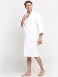 A person standing in a relaxed pose wearing a white, long-sleeved, unisex cotton bathrobe that reaches up to the knees.