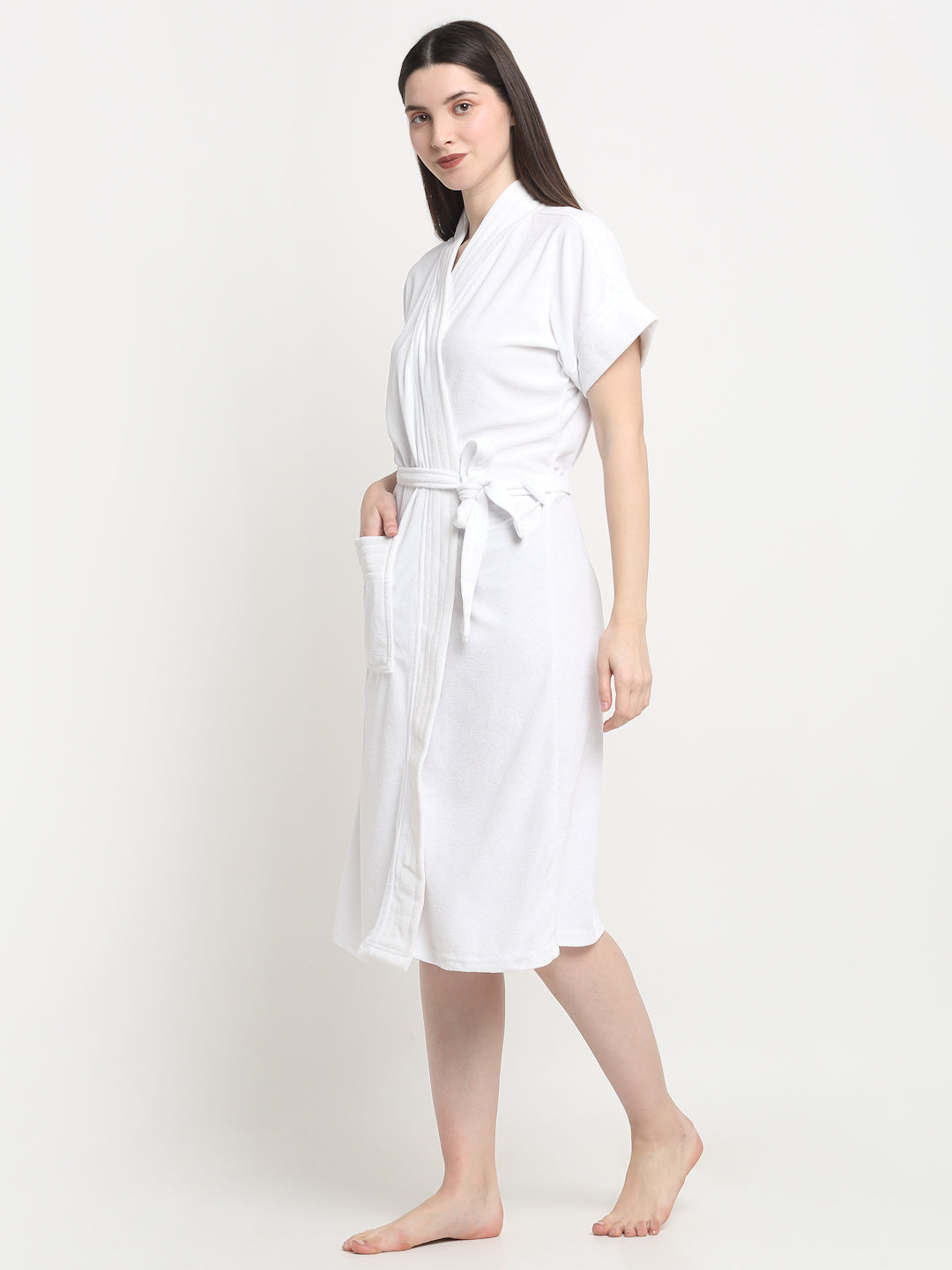 A woman wearing a classic white terry cloth bathrobe with a belt tied around the waist, standing on a white background.