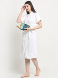A woman stands wearing a white micro terry bathrobe and holding a book