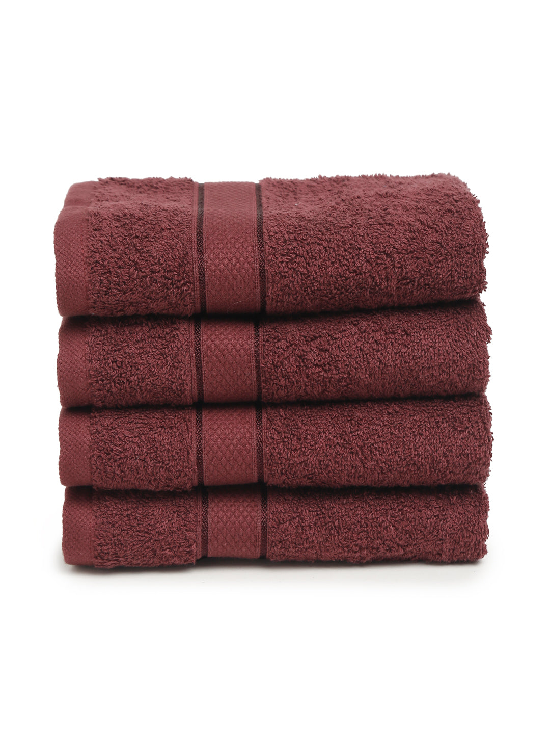 A set of four wine-colored Creeva 100% cotton hand towels, neatly stacked, with a wooden backdrop and a white bowl in the foreground.