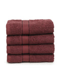 A set of four wine Creeva brand hand towels stacked on a bathroom counter, with a wooden backdrop and a white bowl in the foreground.