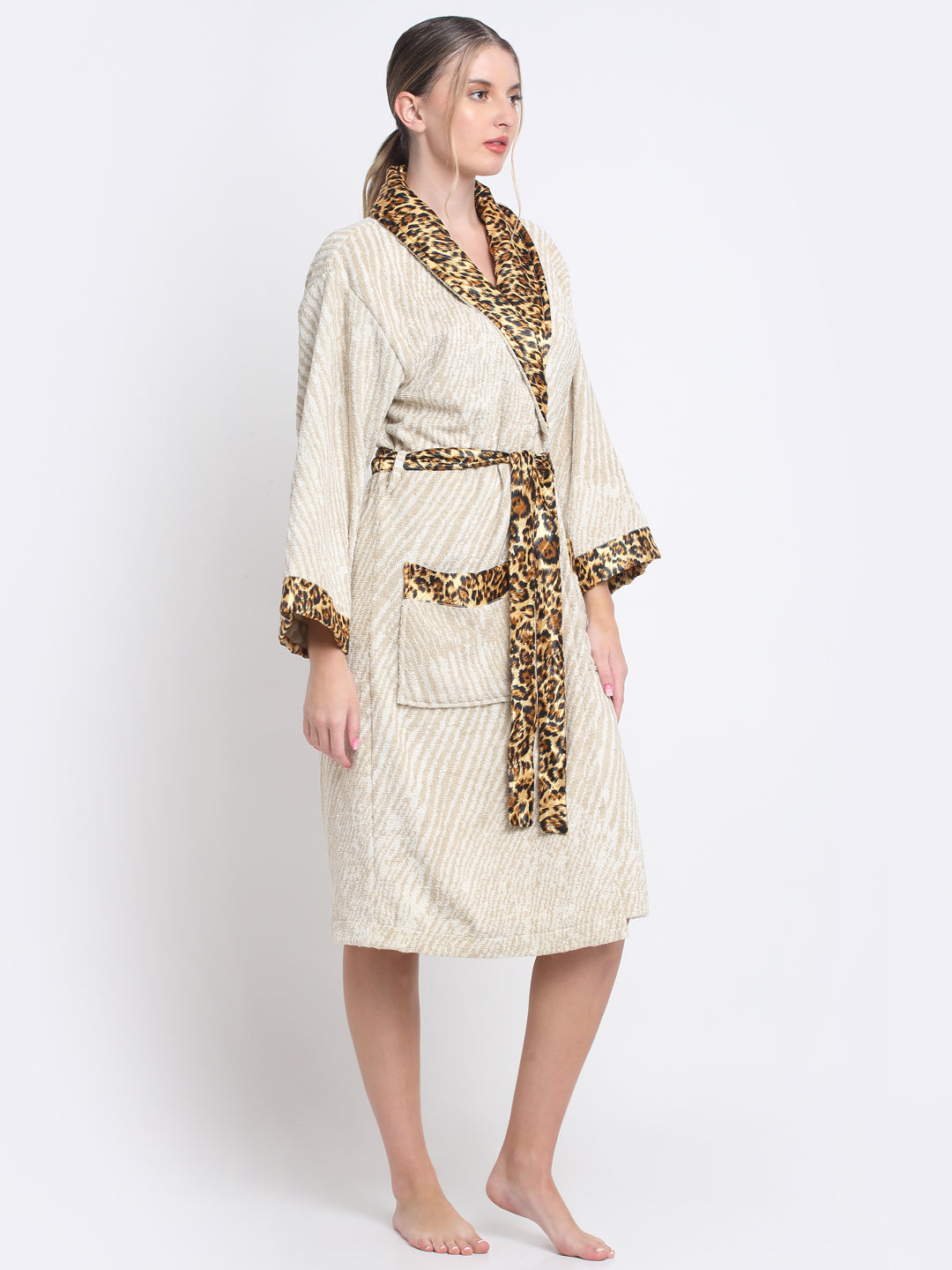 A person wearing a cream and rust leopard print unisex bathrobe with a belt, standing on a stool.