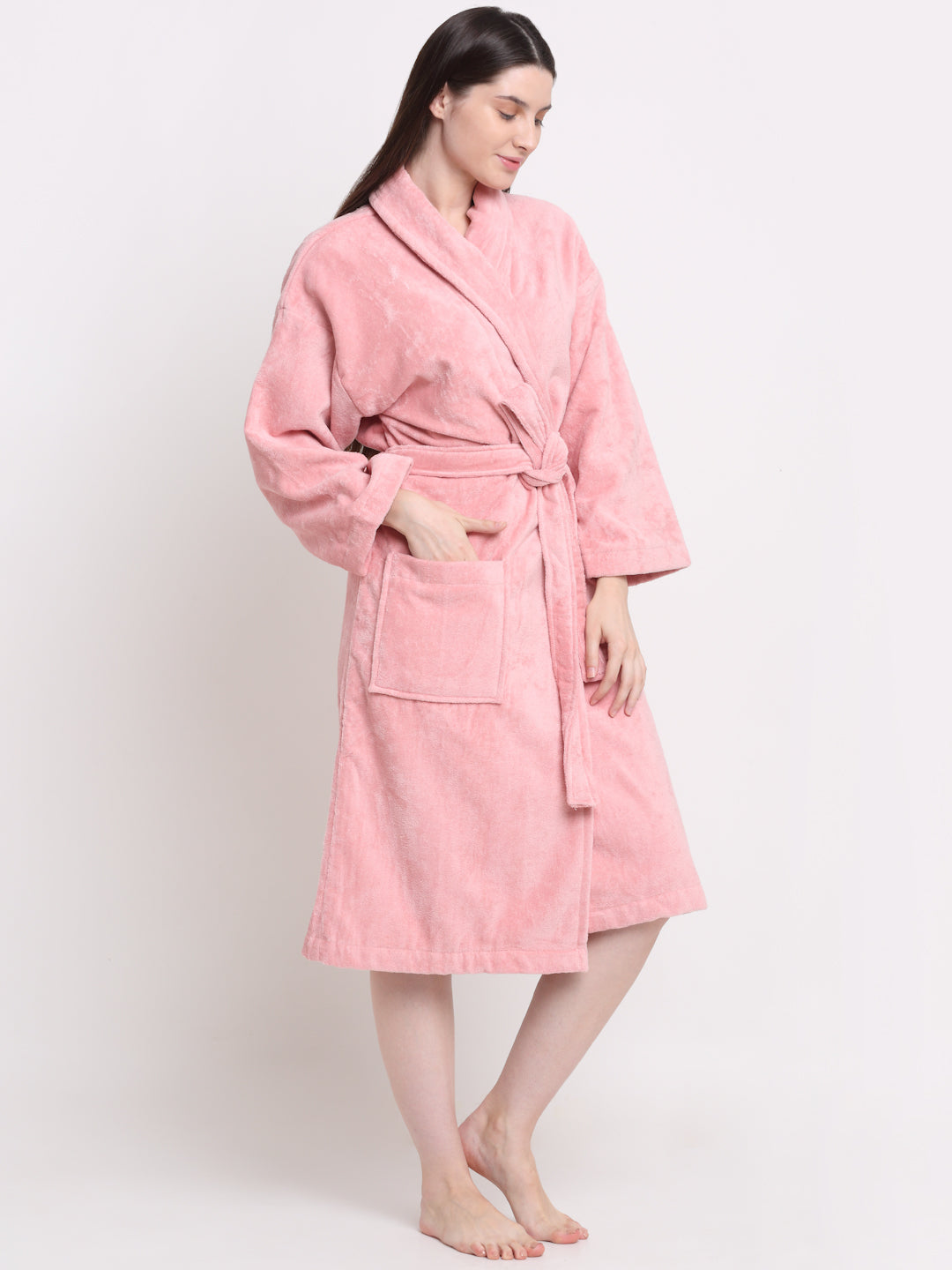 A person wearing a pink unisex cotton bathrobe, standing next to a wooden stool and reading a book.