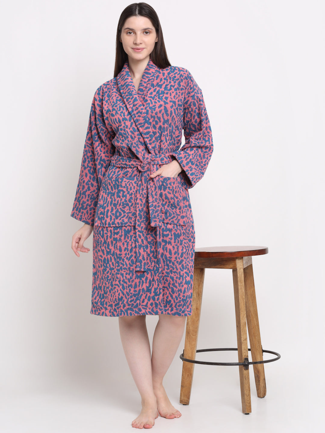 A person standing next to a wooden stool, wearing a pink and blue dotted 100% cotton unisex bathrobe.