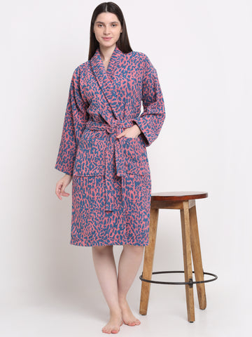 A person standing next to a wooden stool, wearing a pink and blue dotted 100% cotton unisex bathrobe.