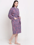 A person standing, wearing a pink and blue colored bathrobe with a rust dotted pattern.