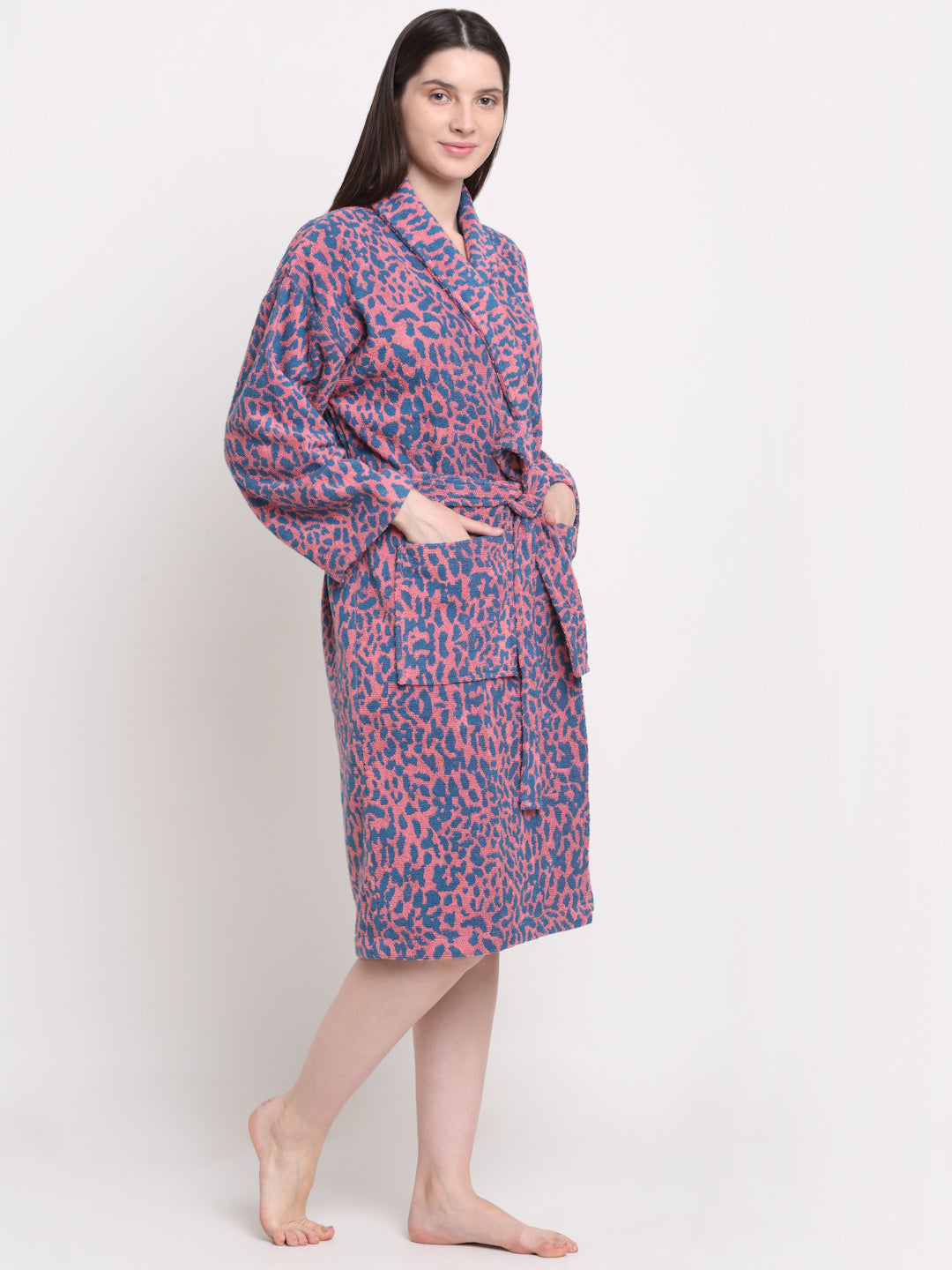 A person standing, wearing a pink and blue colored bathrobe with a rust dotted pattern.