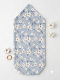 A light blue baby blanket or swaddle with a white and beige floral pattern, laid flat on a white background with small decorative props.