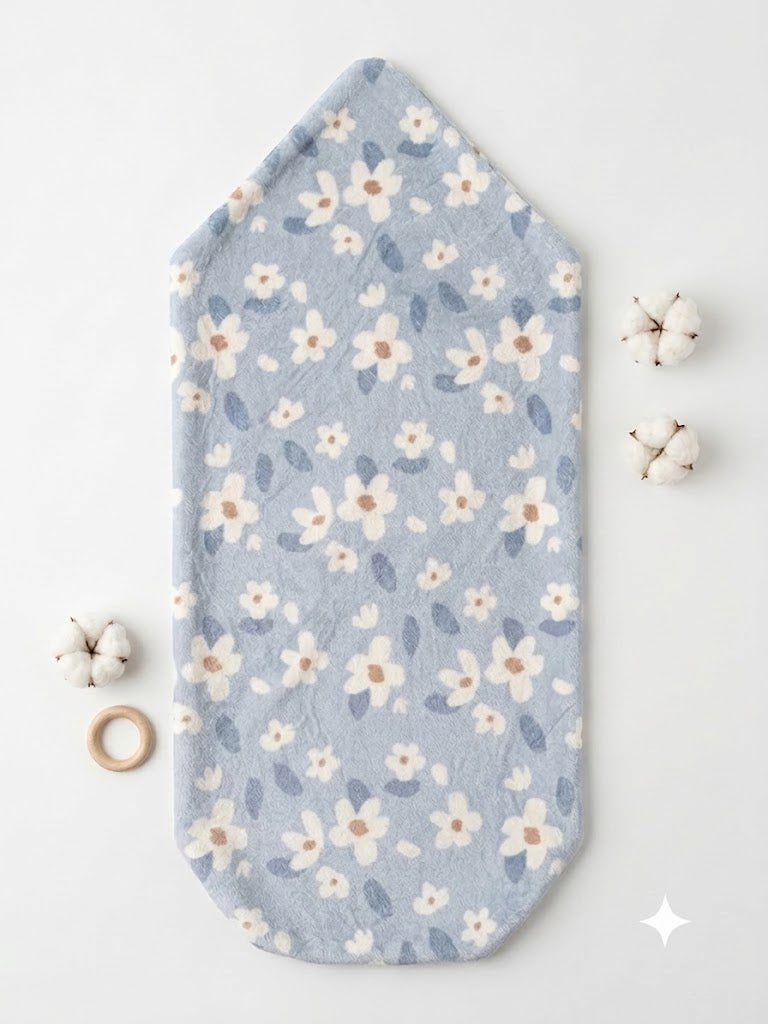 A light blue baby blanket or swaddle with a white and beige floral pattern, laid flat on a white background with small decorative props.