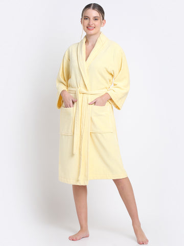 A woman standing and smiling, wearing a yellow 100% cotton luxury bathrobe with a belt, posing against a white background.