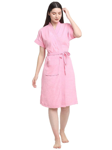 A woman wearing a baby pink terry cloth bathrobe with a tie belt, standing and looking down.