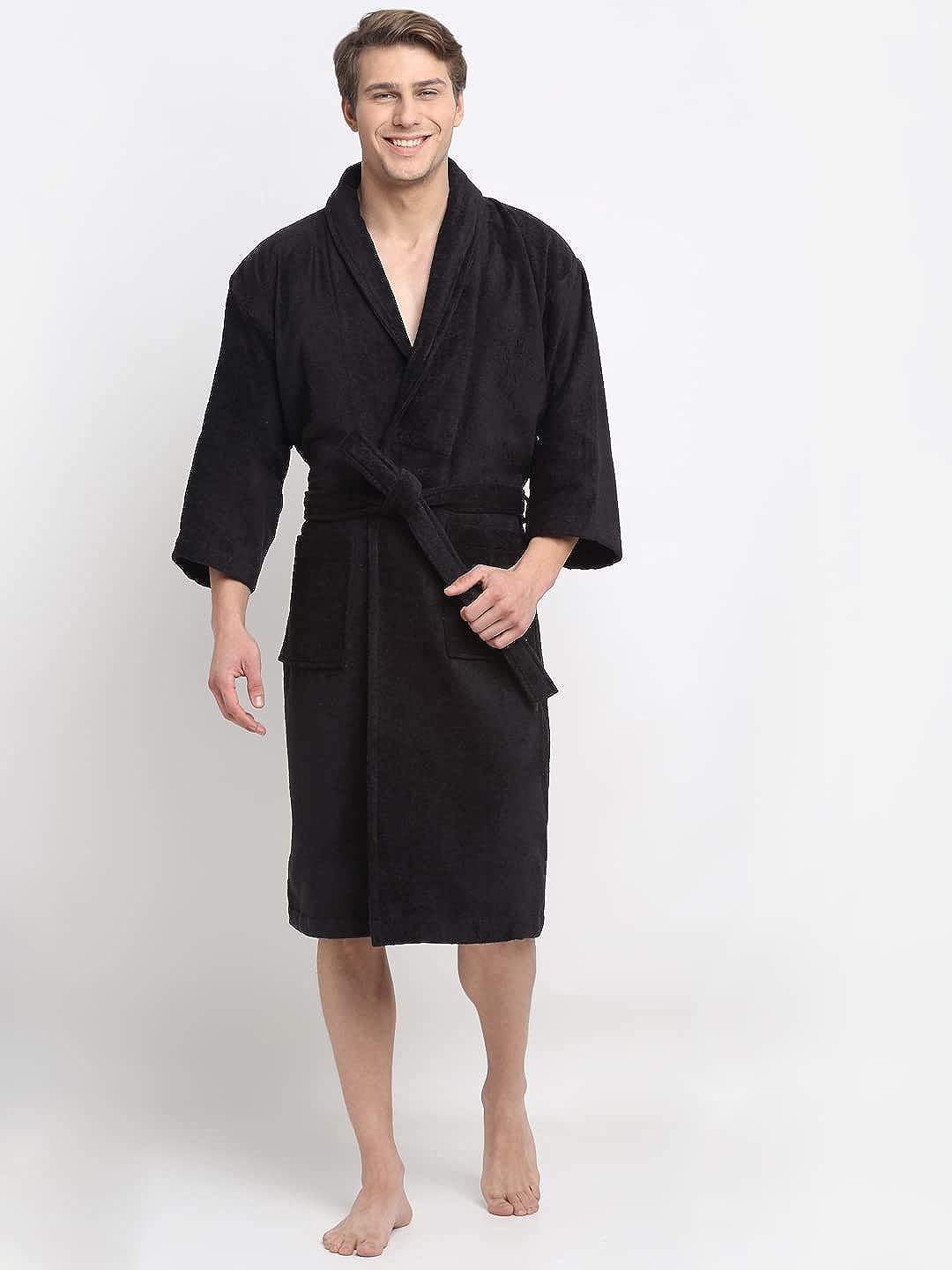 A person standing and smiling, wearing a black 100% cotton unisex bathrobe with a V-neck and a front pocket.