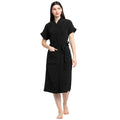 A woman standing and wearing a black terry bathrobe with a belt tied around her waist.