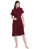 A woman standing wearing a grape wine color turtleneck sleeveless terry bathrobe with a belt.