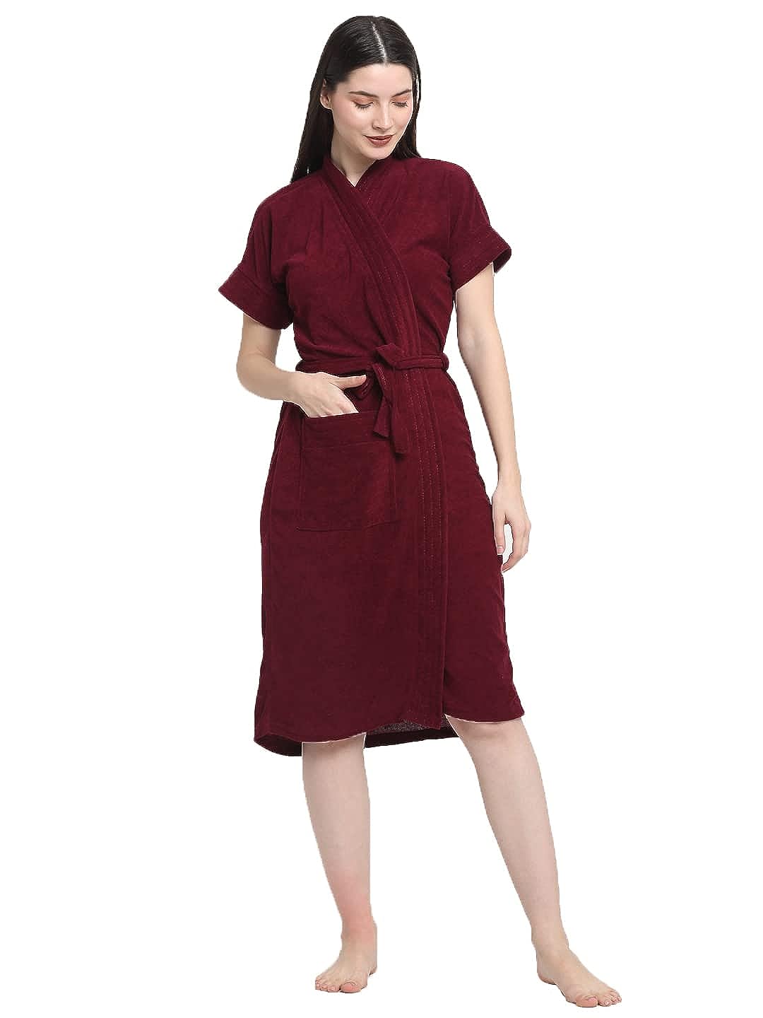 A woman standing wearing a grape wine color turtleneck sleeveless terry bathrobe with a belt.
