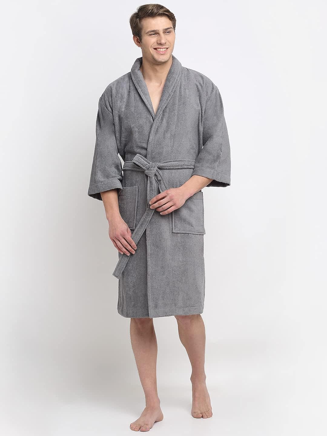 A person standing and smiling, wearing a grey 100% cotton unisex bathrobe with a belt tied around the waist.