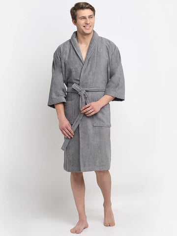 A person standing and smiling, wearing a grey 100% cotton unisex bathrobe with a belt tied around the waist.
