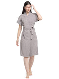 A woman standing, wearing a soft grey terry bathrobe with a V-neck and a tie belt.