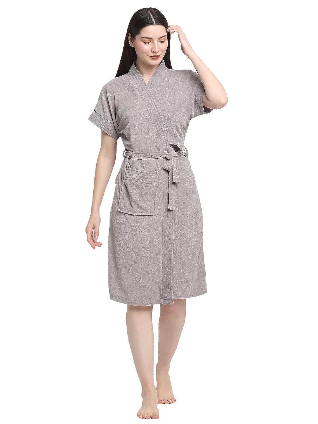 A woman standing, wearing a soft grey terry bathrobe with a V-neck and a tie belt.