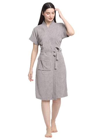 A woman standing, wearing a soft grey terry bathrobe with a V-neck and a tie belt.