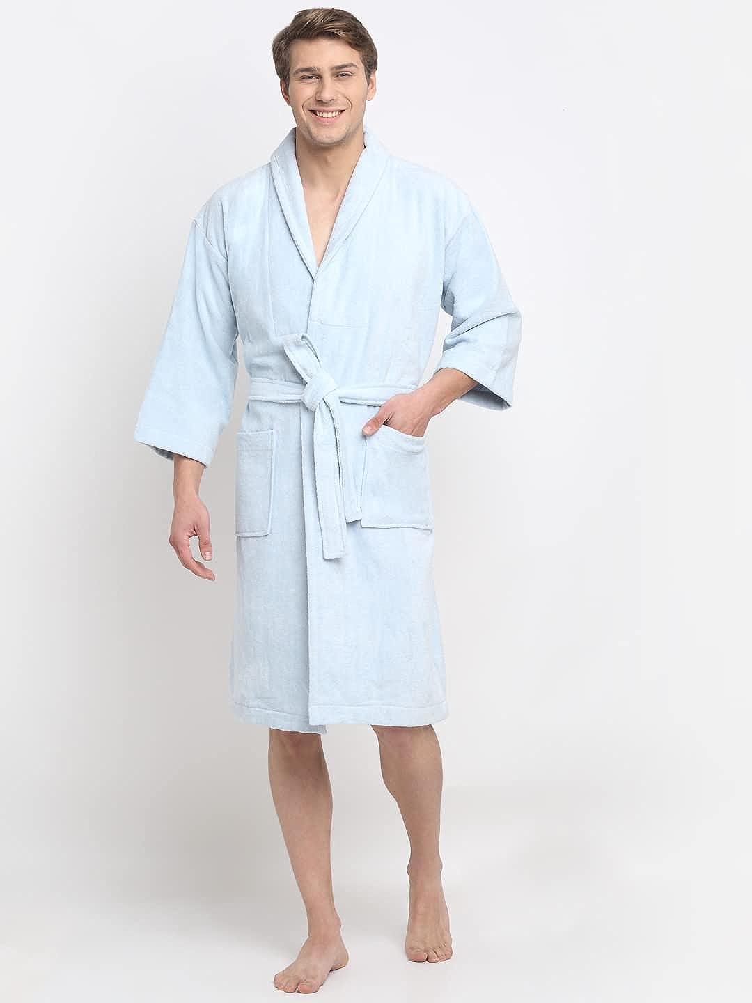 A person standing and smiling, wearing a light blue 100% cotton unisex bathrobe with a belt tied around the waist.