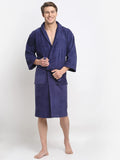 A person standing and smiling, wearing a navy blue 100% cotton unisex bathrobe with a belt tied around the waist.