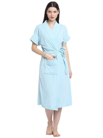 A woman standing and wearing a sky blue terry bathrobe with a belt tied around the waist.