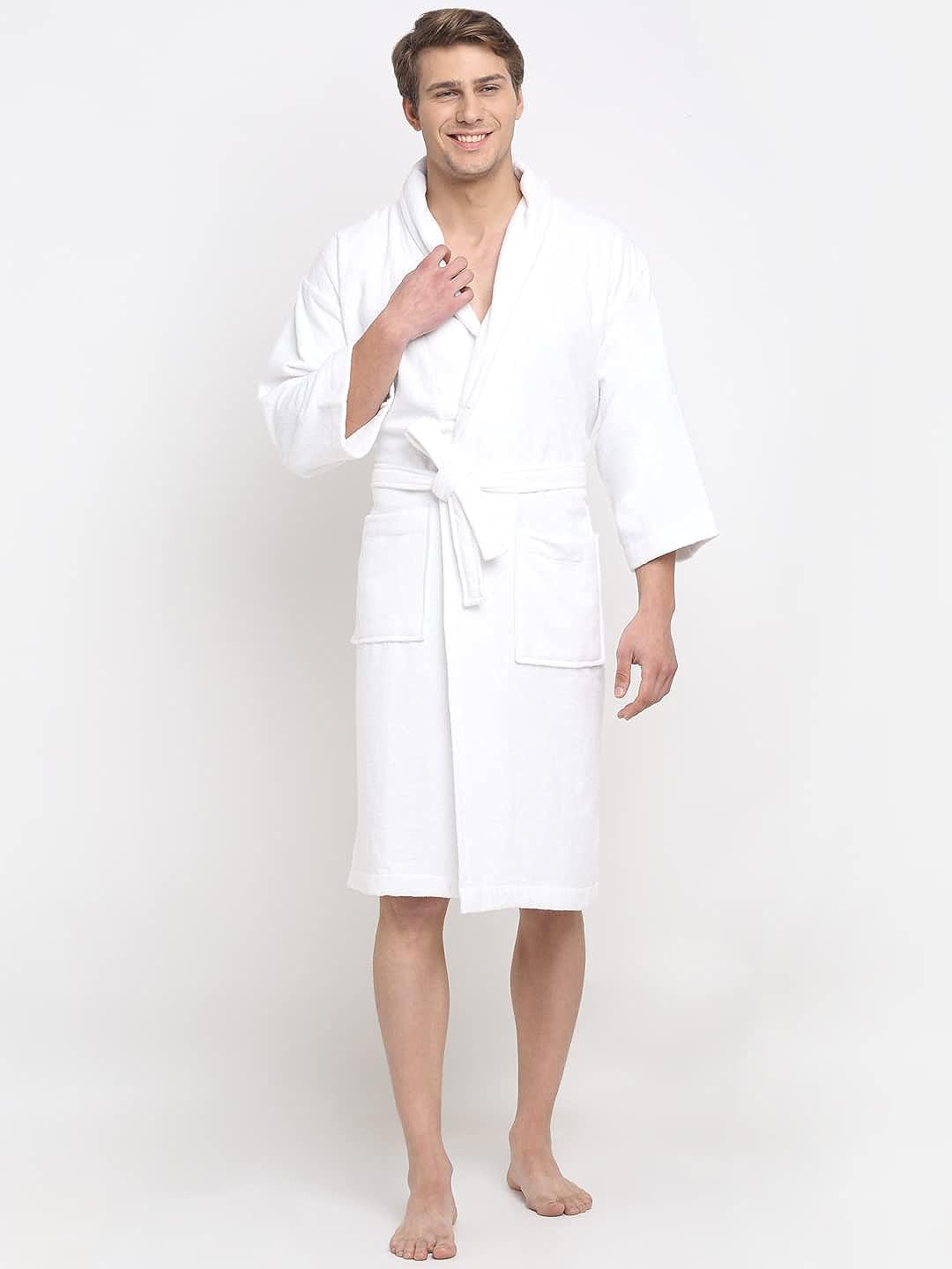 A person standing and smiling, wearing a white 100% cotton unisex bathrobe with a belt tied around the waist.