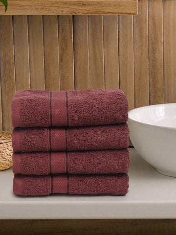 A set of four wine-colored Creeva 100% cotton hand towels, neatly stacked, with a wooden backdrop and a white bowl in the foreground.