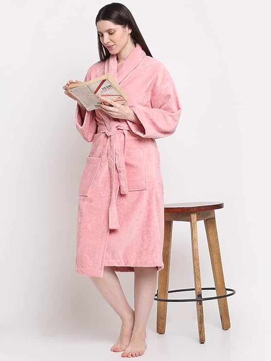 A person wearing a pink unisex cotton bathrobe, standing next to a wooden stool and reading a book.