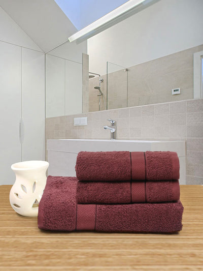 Stack of maroon towels on a wooden surface with a white vase, mirrored bathroom backdrop.
 creeva wine color towels